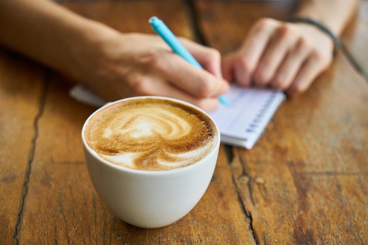 Kaffeetasse und Hände eines Menschen, der sich Notizen macht