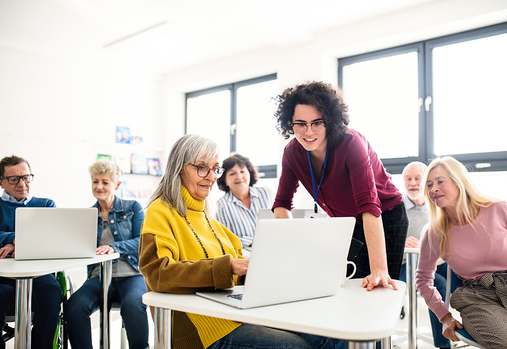 Eine junge Frau unterrichtet im Computerraum eine Seniorengruppe