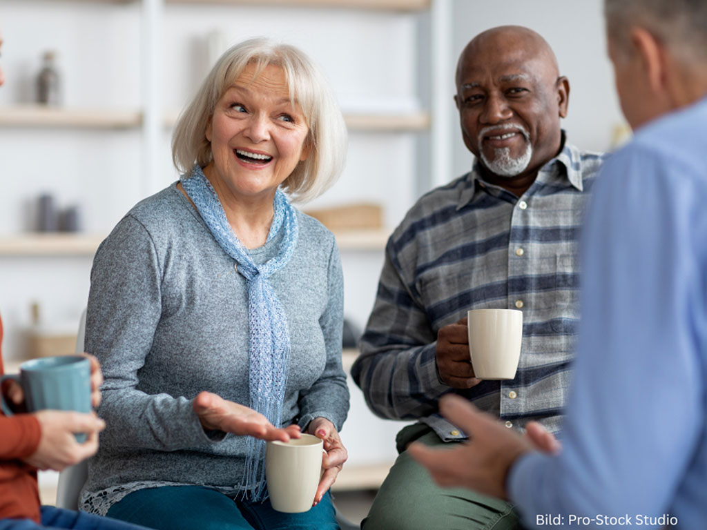 Seniorinnen und Senioren unterhalten sich und haben eine Kaffeetasse in der Hand