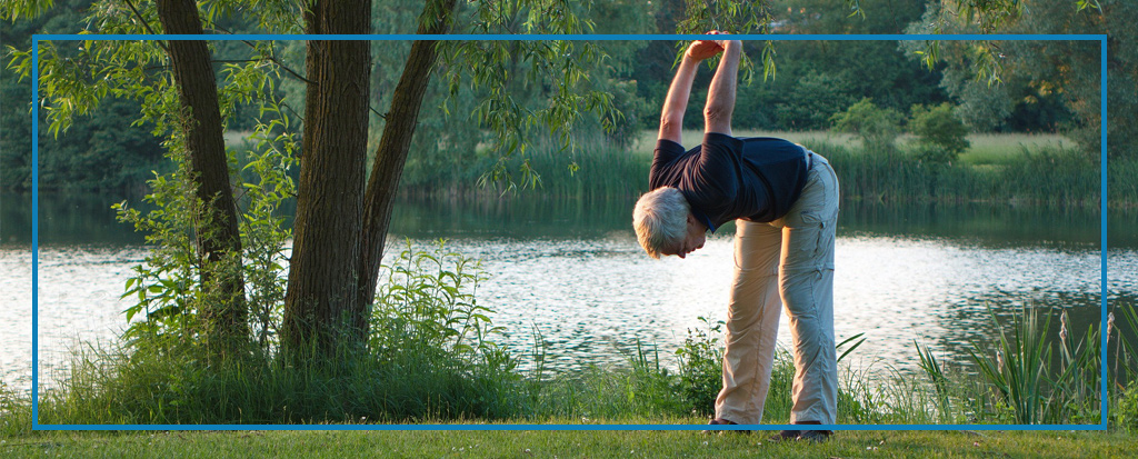 Senior macht eine Gymnastik-Übung an einem See