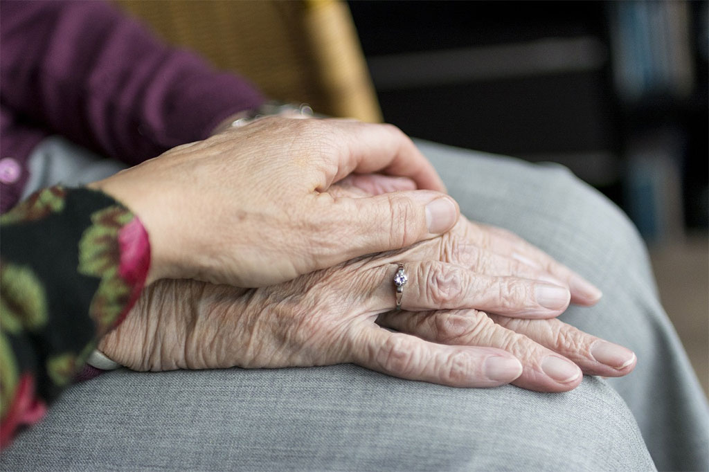 Hand einer jüngeren Person auf Händen einer Seniorin